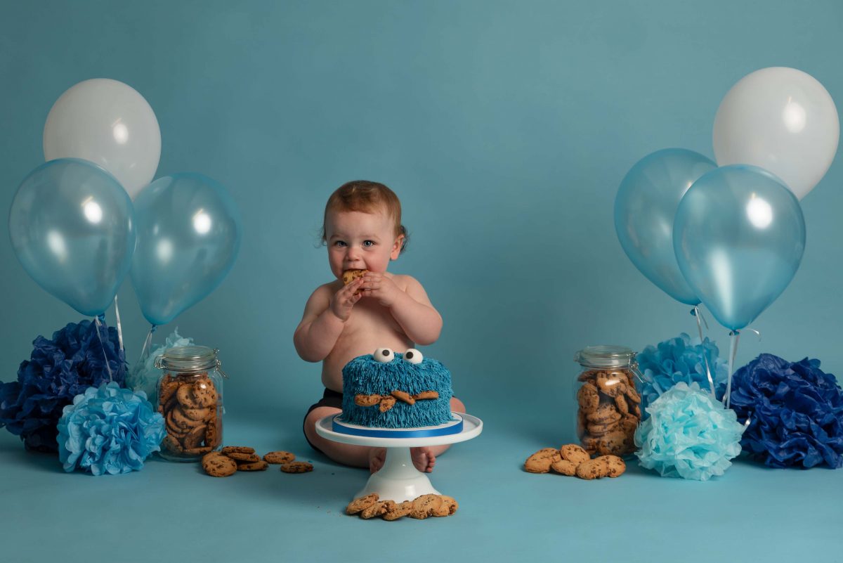 Baby at a cake smash photography session, sat eating birthday cake